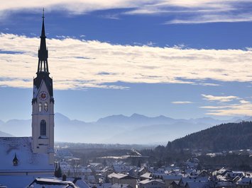 Winterurlaub in Bayern im BERGEBLICK Kirchturm über schneebedecktem Dorf mit Bergen und blauem Himmel im Hintergrund