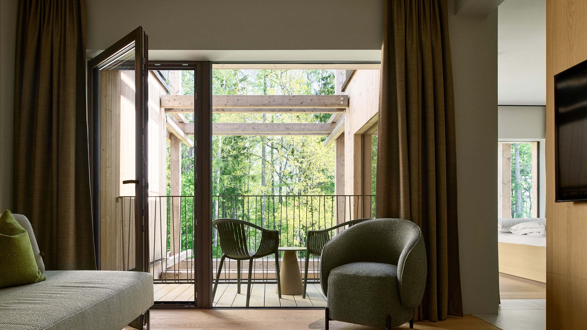 Dein Natururlaub in Bayern: BERGEBLICK Wohnzimmer mit Balkon, grünen Stühlen und Blick auf grüne Bäume
