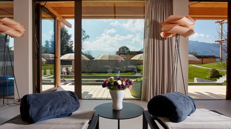 Pictures of a dream holiday in Bad Tölz Two lounge chairs with blue towels and flower vase by large glass window overlooking outdoor area