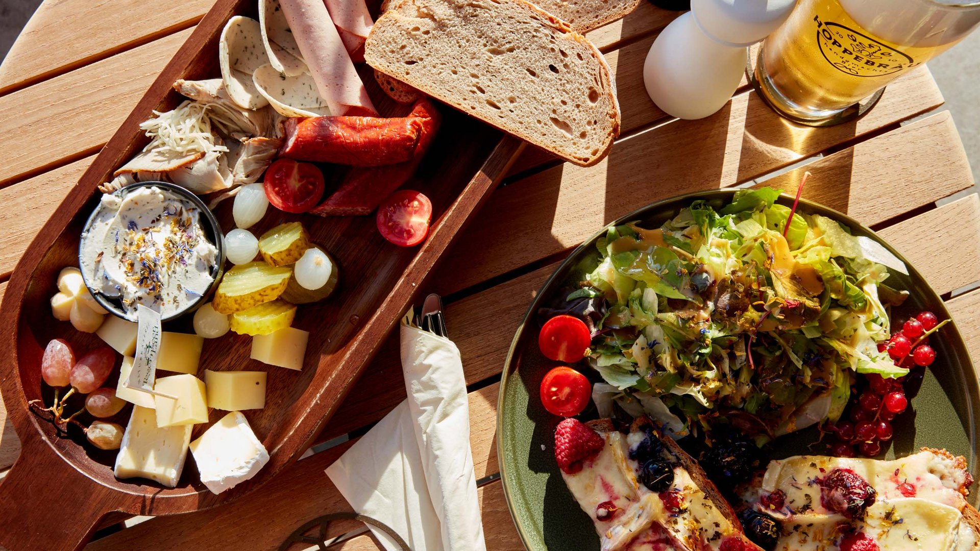 Deine Lounge für Business & Genuss Brett mit Wurst, Käse, Brot, Salat, und Glas Bier auf Holztisch