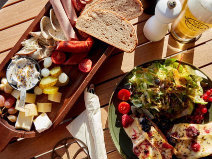 Bad Tölz: Hotel mit regionalem Frühstück Brett mit Wurst, Käse, Brot, Salat, und Glas Bier auf Holztisch