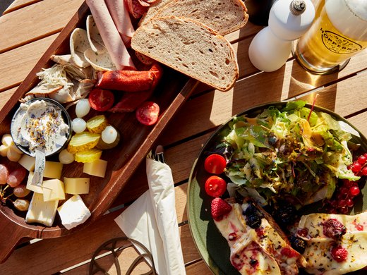 Was ist im Hotel BERGEBLICK inklusive? Brett mit Wurst, Käse, Brot, Salat, und Glas Bier auf Holztisch