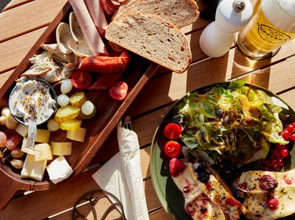 Bad Tölz: Hotel mit regionalem Frühstück Brett mit Wurst, Käse, Brot, Salat, und Glas Bier auf Holztisch