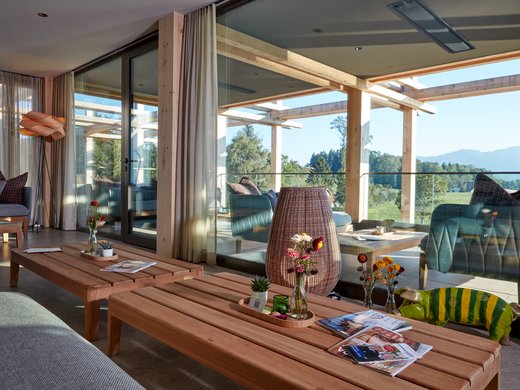 Willkommen im Boutiquehotel in Bayern Gemütlicher Wohnbereich mit Holztischen, Dekoration und Ausblick auf Balkon und Natur