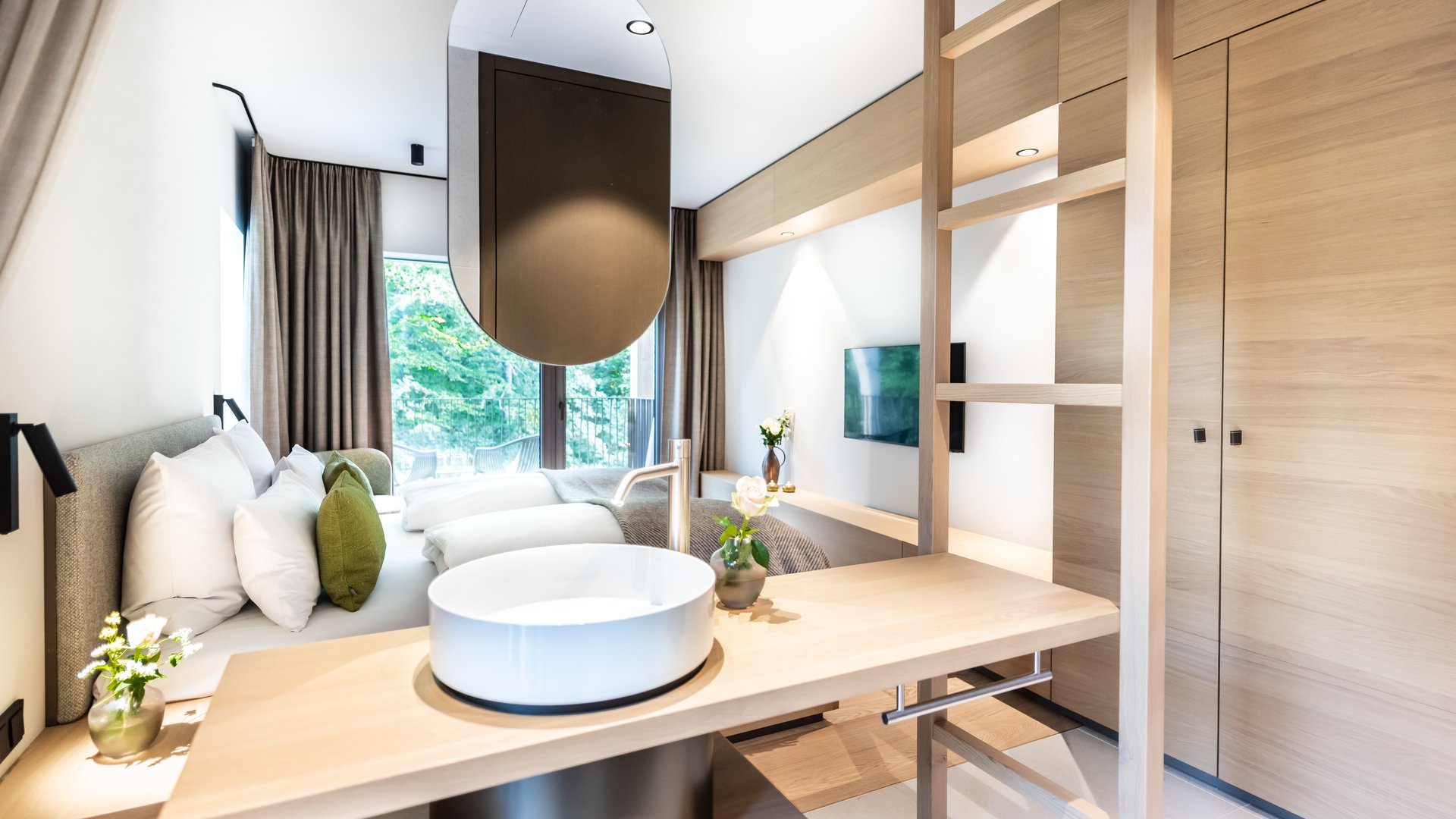 Sonja Sindlhauser Modernes Hotelzimmer mit Holzdetails, Waschbecken und Doppelbett mit grünen Kissen