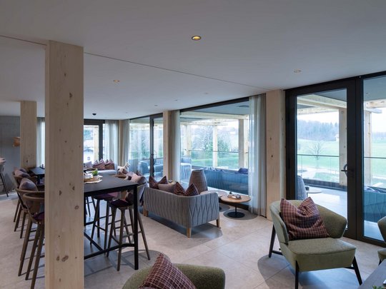 Wissenswertes aus Bad Tölz Moderner Wohnraum mit Sofas, Tischen und großen Fenstern mit Blick auf die Landschaft