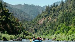 Urlaub im Aktivhotel in Bayern Gruppe von Menschen beim Wildwasser-Rafting in einem Fluss umgeben von bewaldeten Bergen