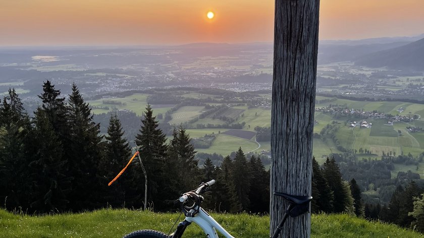 Vorfreude auf die schönste Freude Mountainbike lehnt an einem Holzmast mit Blick auf Sonnenuntergang und Tal