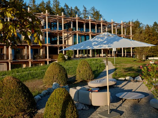 Was ist im Hotel BERGEBLICK inklusive? Moderne Unterkunft mit Sonnenschirm und Gartenbänken an einem sonnigen Tag