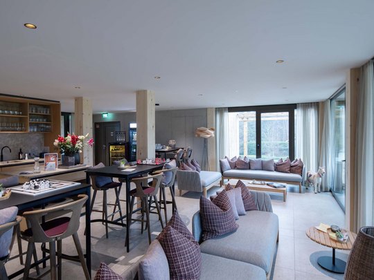 Wissenswertes aus Bad Tölz Moderne Lounge mit Sofas, Tischen, Stühlen und großen Fenstern
