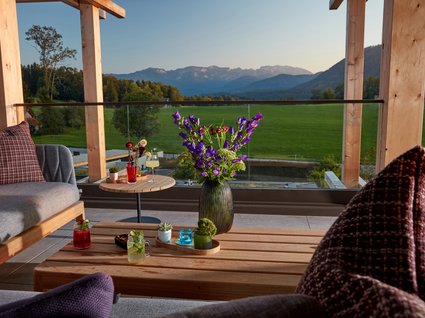 Dein Natururlaub in Bayern: BERGEBLICK Terrasse mit Sofa, Tisch, Blumen und Bergblick im Sonnenuntergang