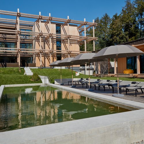 Wellness in Bad Tölz Modern wooden building with pool, sun loungers, and umbrellas in the garden