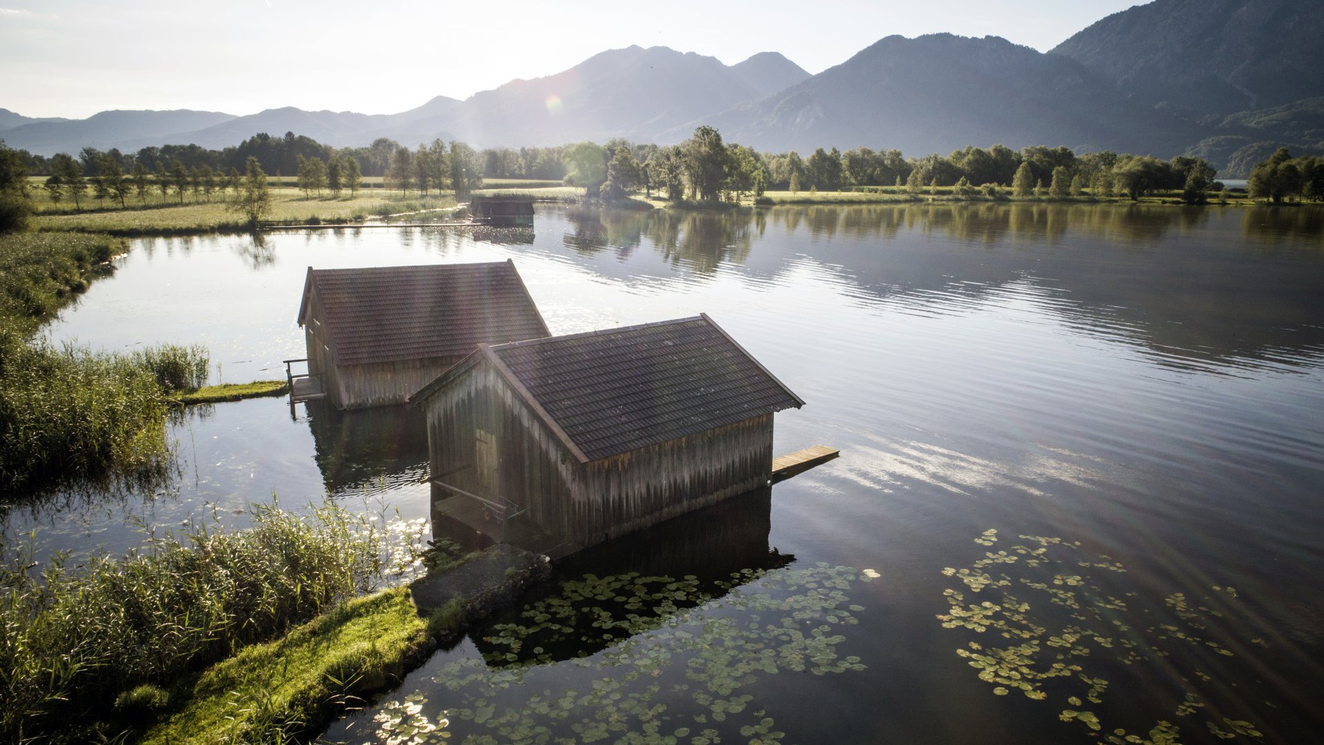 Your active summer holiday in Bavaria Two boathouses on a calm lake with mountains in the background at sunlight