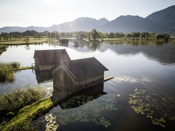 Urlaub im Aktivhotel in Bayern Zwei Boots-Hütten am ruhigen See mit Bergkulisse bei Sonnenlicht