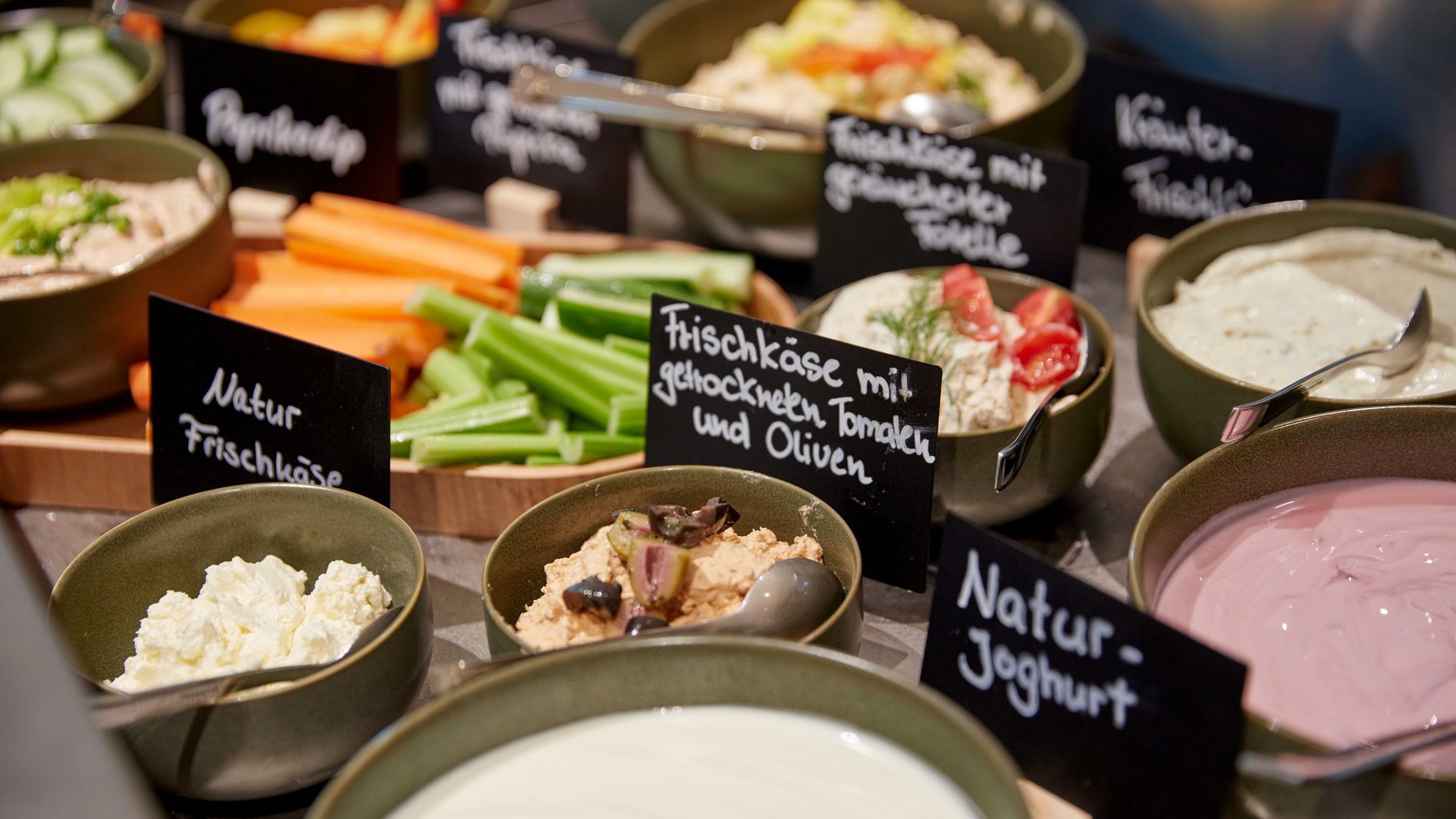 Bad Tölz: Hotel mit regionalem Frühstück Verschiedene Frischkäse und Gemüse in Schalen mit Beschriftungen auf einem Buffet