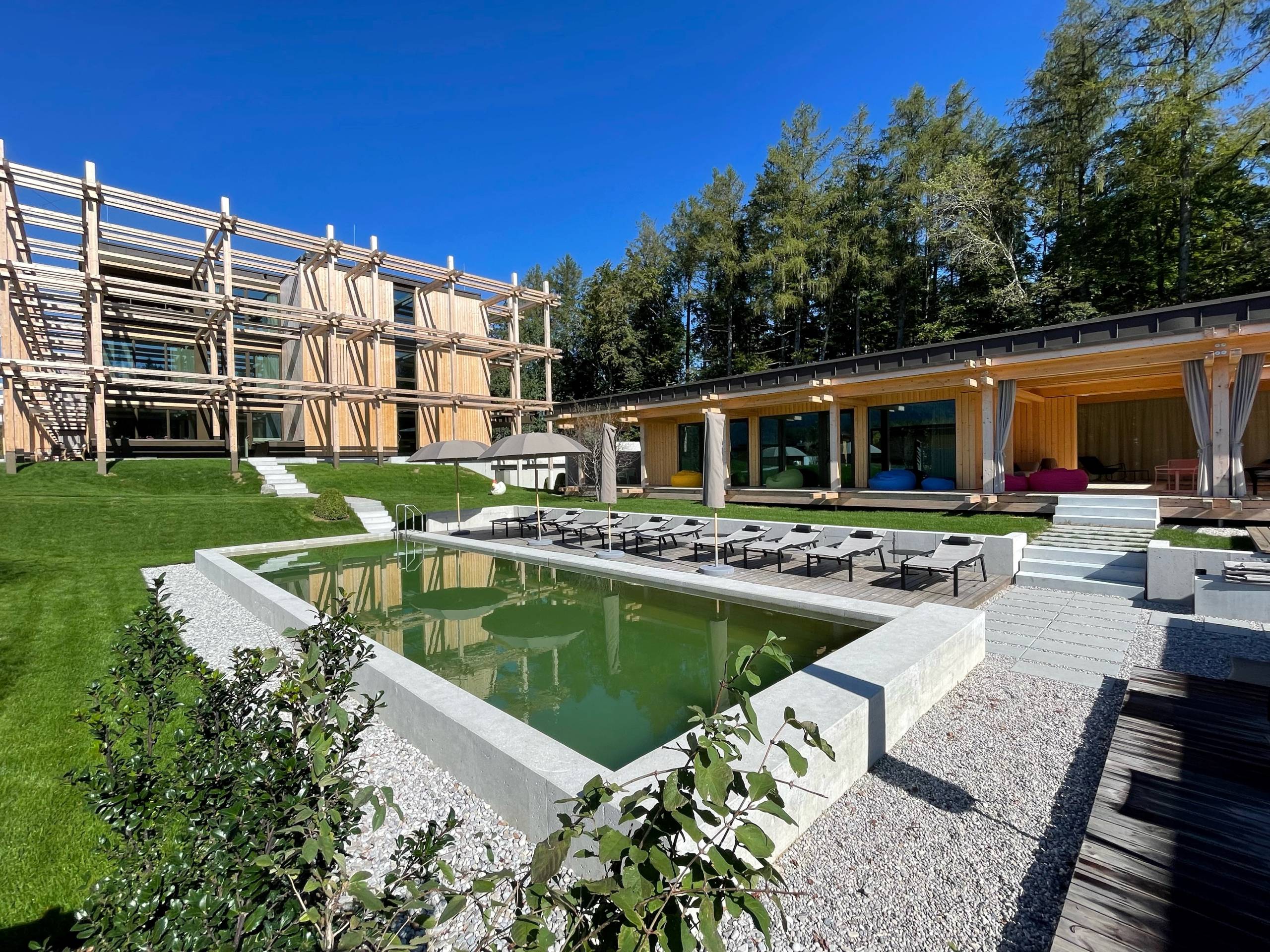 Hotel BERGEBLICK für Wellness in Bad Tölz Moderner Holzbauten mit grünem Garten und kleinem Teich bei sonnigem Wetter